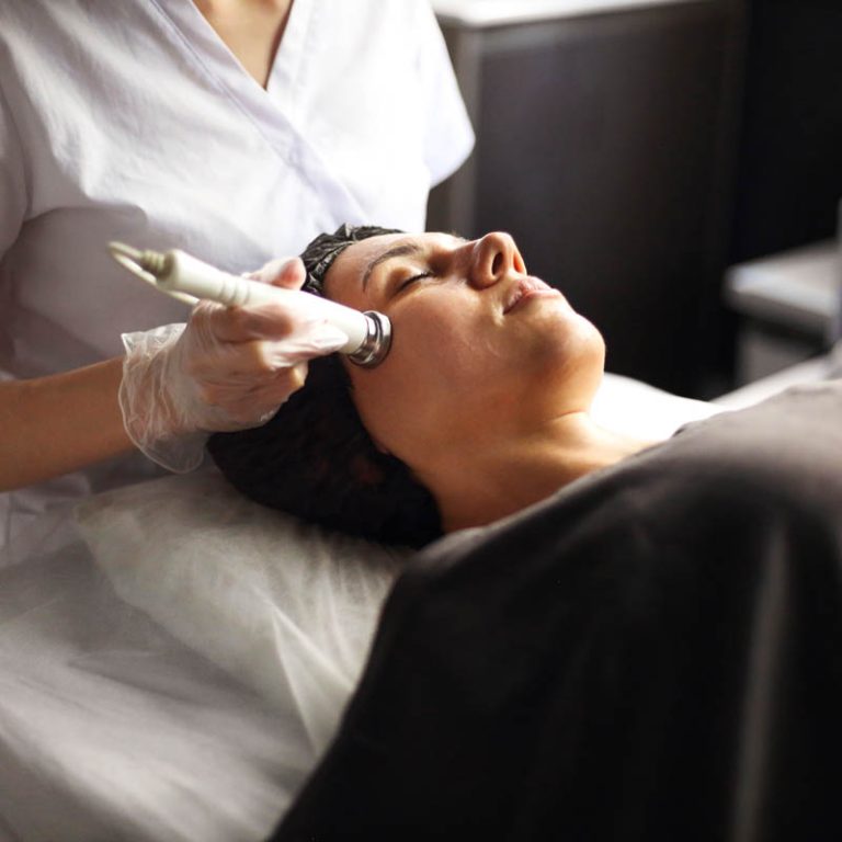 Cosmetician using modern machine for radiofrequency therapy on face of female client