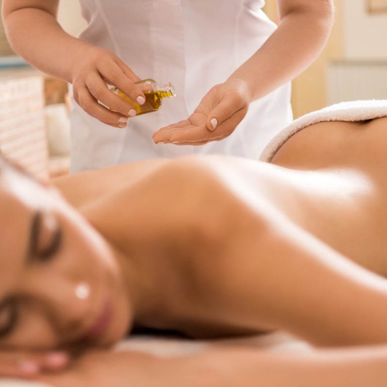 massage therapist making massage with body oil for woman in spa salon