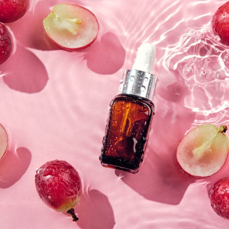 Organic cosmetics with grape seed oil and herbal ingredients. Zero Waste Winemaking. Skincare cosmetic product, grapes and water splashes on pink background.